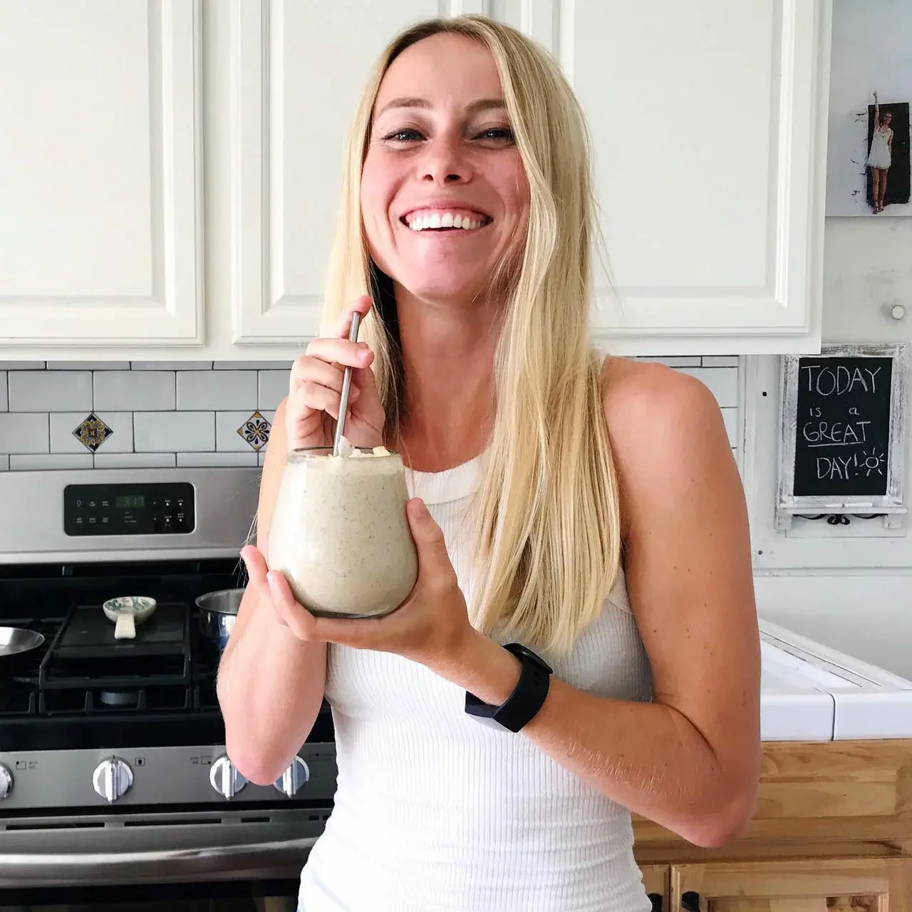Autumn, author of Autumn Elle Nutrition, standing in kitchen drinking a protein shake and smiling.