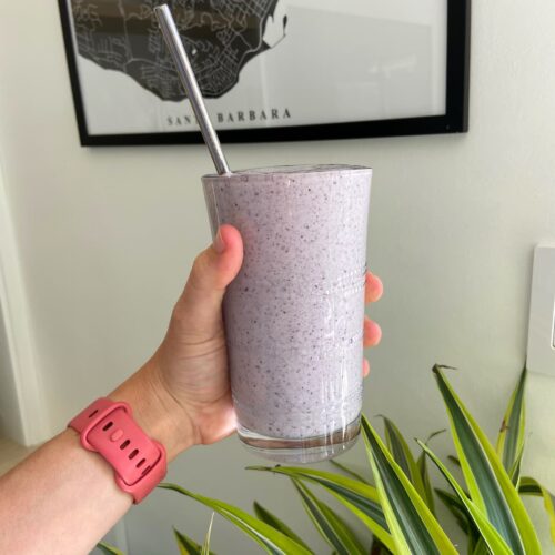 blueberry protein shake held up in front of a green plant and picture