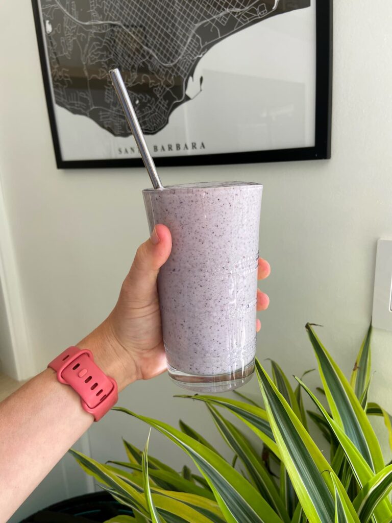 blueberry protein shake held up in front of a green plant and picture
