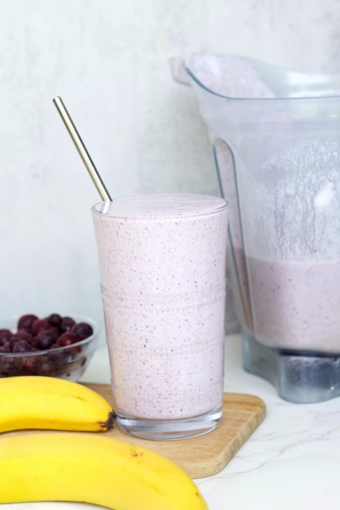 blueberry protein shake in a glass with the blender behind it