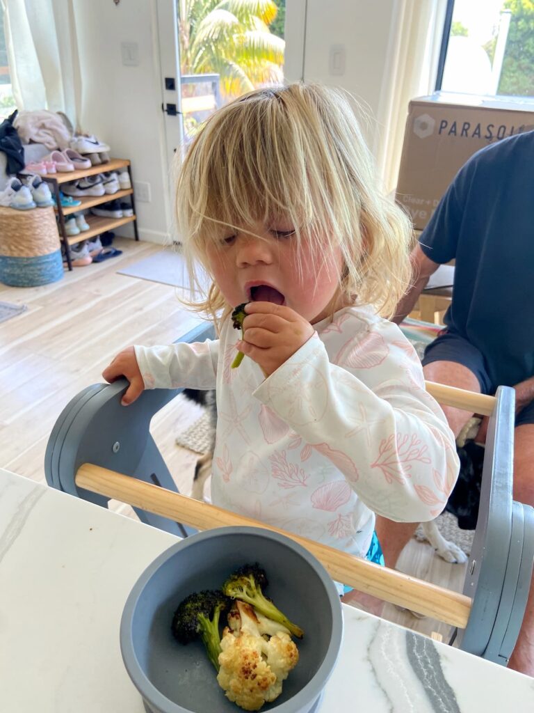 toddler girl eating roasted broccoli and cauliflower
