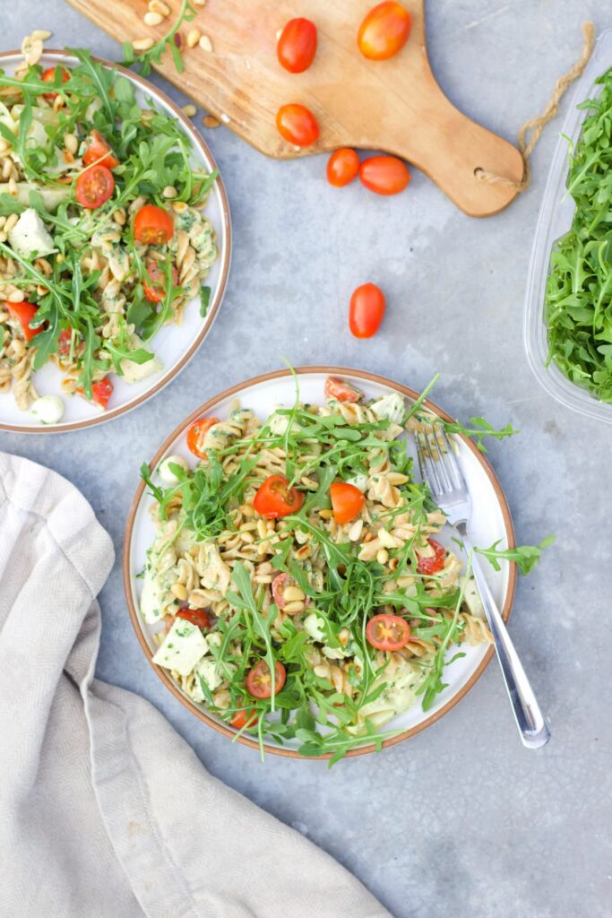 high protein pesto pasta salad with two plates and a cutting board