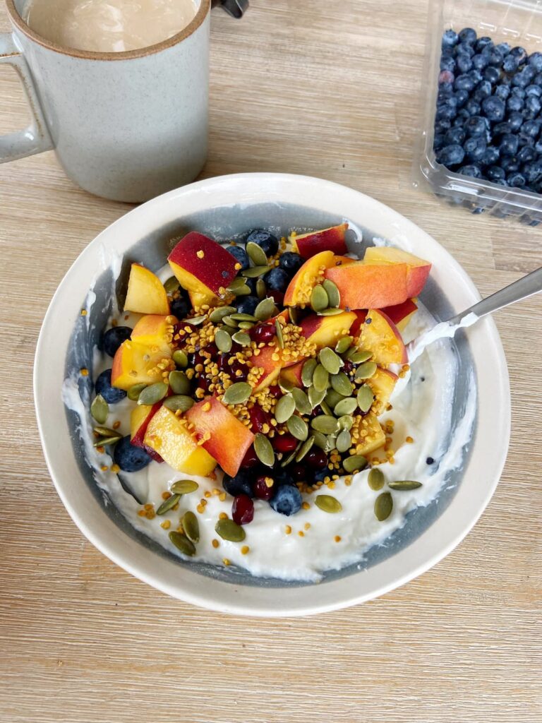 High protein yogurt bowl with peaches, blueberries, pumpkin seeds and bee pollen