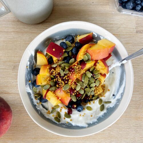 High protein yogurt bowl with peaches, blueberries, pumpkin seeds and bee pollen