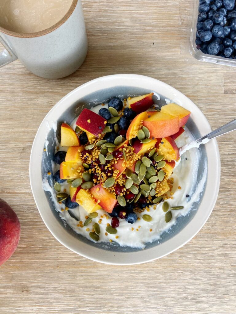 High protein yogurt bowl with peaches, blueberries, pumpkin seeds and bee pollen