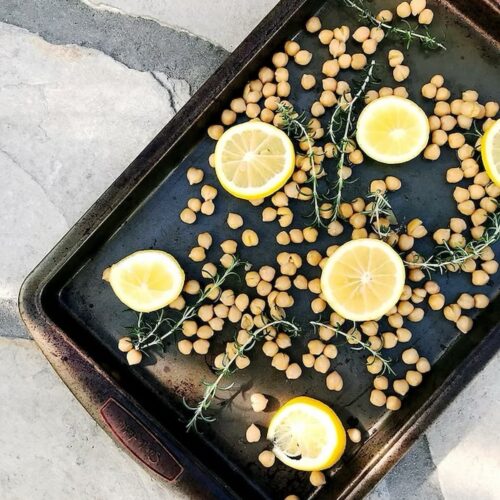 chickpeas on a baking sheet with lemons and rosemary