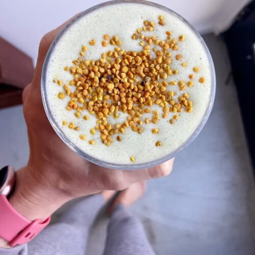 high protein green smoothie in a glass with bee pollen topping