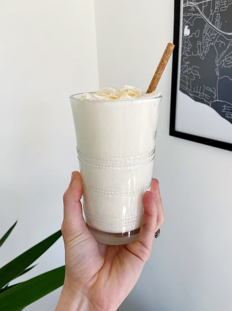 pineapple protein smoothie in a glass with coconut flakes on top