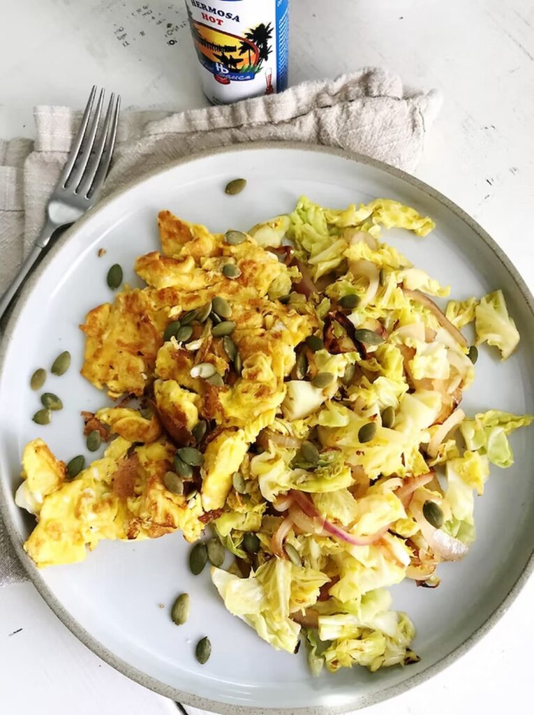 scrambled eggs and cabbage on a plate with pumpkin seeds and a fork