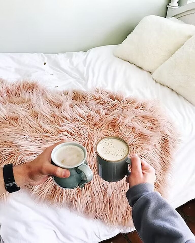 two cups of coffee cheersing in front of a bed
