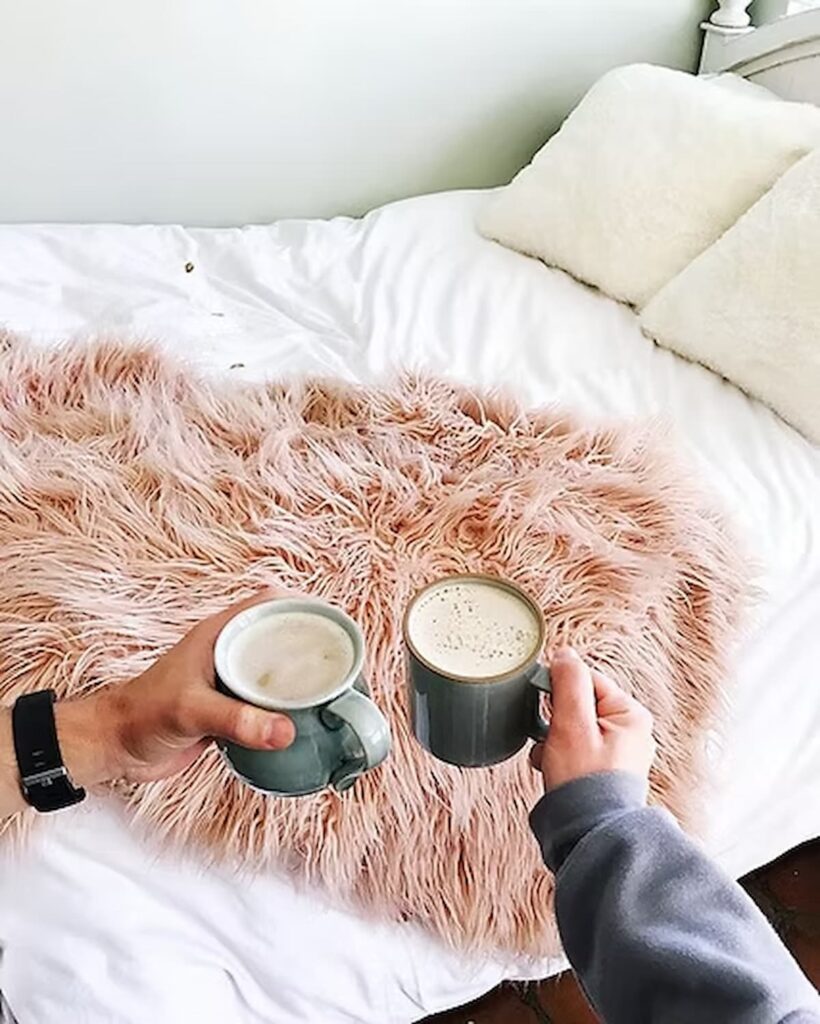 two cups of coffee cheersing in front of a bed