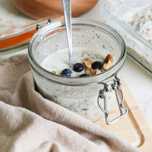 high protein overnight oats in a glass jar with a spoon and blueberry and walnut toppings