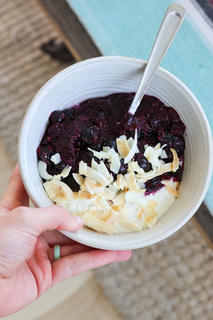 white bowl filled with cottage cheese, warmed blueberries and coconut flakes on top