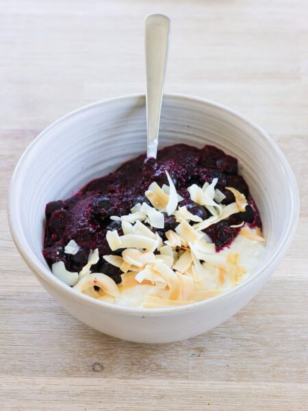 white bowl filled with cottage cheese, warmed blueberries and coconut flakes on top