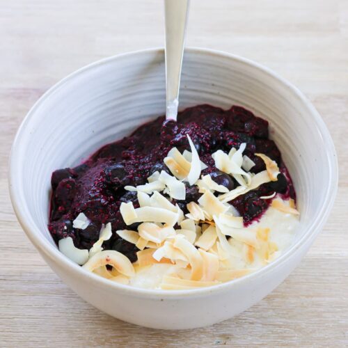 white bowl filled with cottage cheese, warmed blueberries and coconut flakes on top
