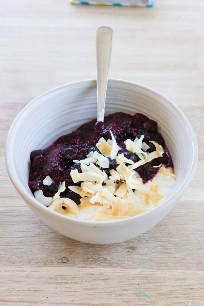 white bowl filled with cottage cheese, warmed blueberries and coconut flakes on top